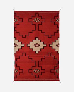 a red rug with white and brown designs on the bottom, in front of a gray background