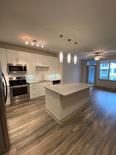 an empty kitchen and living room with wood flooring, stainless steel appliances and white cabinets