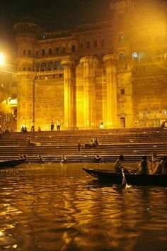 some people are sitting on small boats in the water at night near an old building