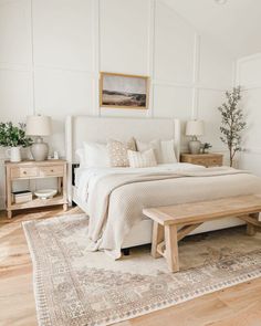 a bedroom with white walls and wood flooring has a large bed, two nightstands, and a bench in front of the bed