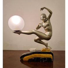 a bronze statue holding a white ball on top of a wooden table next to a lamp