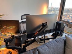 two computer monitors sitting on top of a desk in front of a window with city view