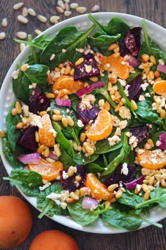 a salad with oranges, spinach and nuts on a plate next to some other vegetables