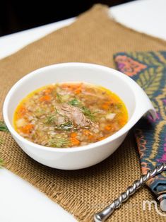 a white bowl filled with soup on top of a place mat next to a spoon