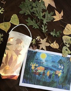 a paper lantern sitting on top of a wooden table next to leaves and a painting