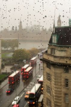 rain drops on the window as buses drive down the street in front of buildings and traffic