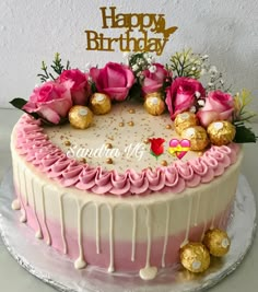 a birthday cake with pink and white frosting, gold decorations and flowers on top