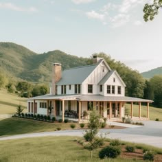 a large white house sitting in the middle of a lush green field with mountains behind it