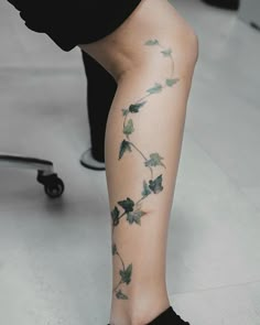 a woman's legs with tattoos on them and one leg is covered in leaves