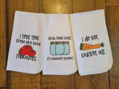 three kitchen towels with words on them