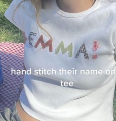 a woman sitting on the grass wearing a white t - shirt that says mama and stitch their name on it