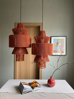 an orange lamp hanging over a table next to a book and vase on top of it