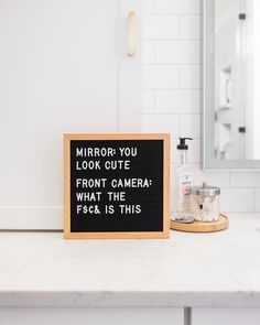 a bathroom counter with a mirror, soap dispenser and sign that says mirror you look cute front camera what the fsc is this?