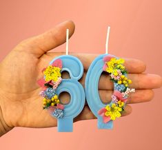 a hand is holding two birthday candles decorated with flowers and the number six on them