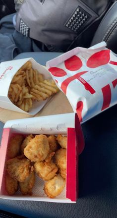 some food is sitting in a box on the seat belt and someone is holding a backpack behind it