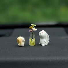 two small plastic animals sitting on top of a car dashboard next to a vase with flowers in it