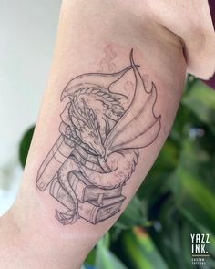 a woman's arm with a tattoo on it that has an image of a dragon holding a book