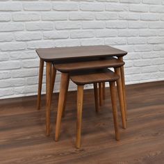 three wooden tables sitting on top of a hard wood floor next to a white brick wall