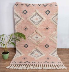 a pink and grey rug with fringes on the floor next to a potted plant