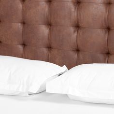 two white pillows on top of a brown leather headboard with buttons and piping