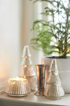 three small christmas trees are sitting on a mantle with candles in front of the windowsill