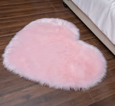 a pink heart shaped rug sitting on top of a wooden floor next to a bed