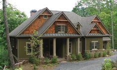 a large house in the woods with lots of trees and bushes around it's front entrance