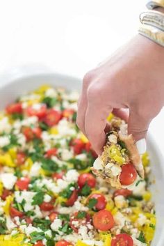 a person holding a slice of pizza with tomatoes and other toppings in a white casserole dish