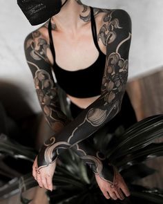 a woman with tattoos on her arms and arm is sitting in front of a plant