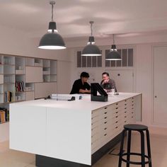 two people sitting at a counter in a room with bookshelves and shelves on the wall