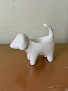 a small white dog shaped vase sitting on top of a wooden table next to a wall