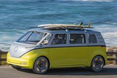 a yellow and white van with surfboards on top driving down the road by the ocean