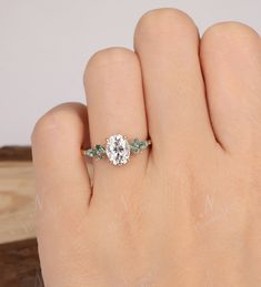 a woman's hand with a ring on it that has a diamond and green leaves