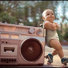 a baby standing next to a boombox on top of a skateboard in the street