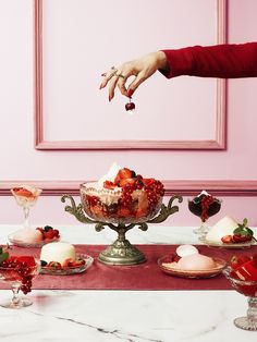 a woman reaching for some fruit on top of a cake stand with other desserts