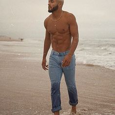 a shirtless man standing on the beach next to the ocean