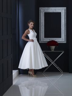 a woman standing in front of a mirror wearing a white dress with bow at the waist