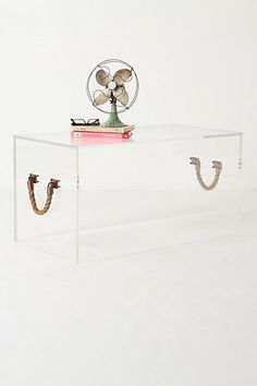 a glass table with two books and a fan on top, in front of a white wall