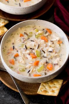 two bowls filled with soup and crackers on top of a wooden plate next to each other