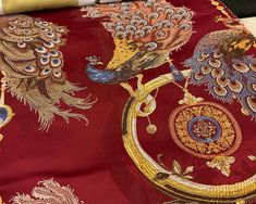 a close up of a red cloth with peacocks on it and gold trimming