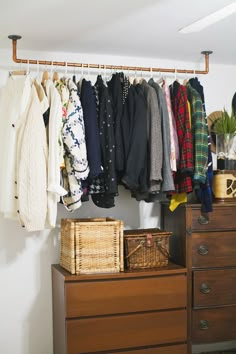 an organized closet with clothes hanging on the rail and baskets in front of it,