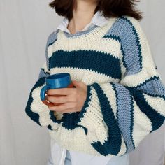 a woman holding a blue cup and wearing a white striped sweater with stripes on it