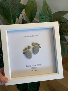 a person holding up a white frame with two rocks in it and the words welcome to the world