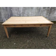 a wooden table with two drawers sitting on the ground in front of a concrete wall