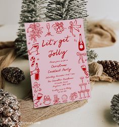 a pink card with red writing on it sitting next to pine cones and other decorations