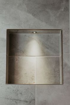 a square mirror mounted on the wall above a toilet paper dispenser in a bathroom