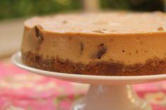 a cheesecake sitting on top of a white cake plate next to a pink table cloth