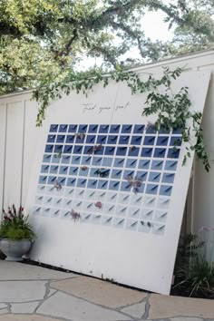 a white board with blue squares on it sitting next to a potted plant and tree