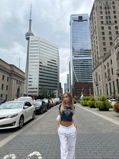 a woman standing in the middle of a street with cars parked on both sides and tall buildings behind her