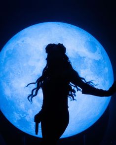 the silhouette of a woman with long hair standing in front of a blue full moon